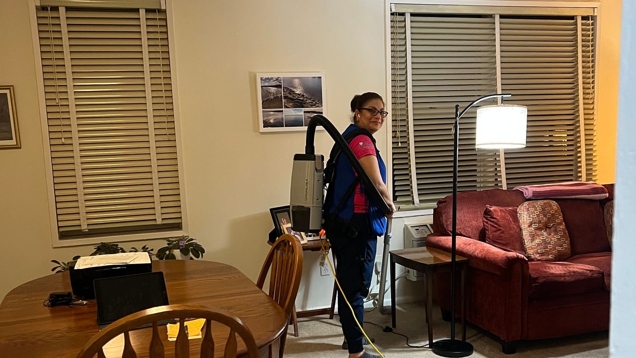 A Nissi's Cleaning Service team member vacuuming a living room with a backpack vacuum